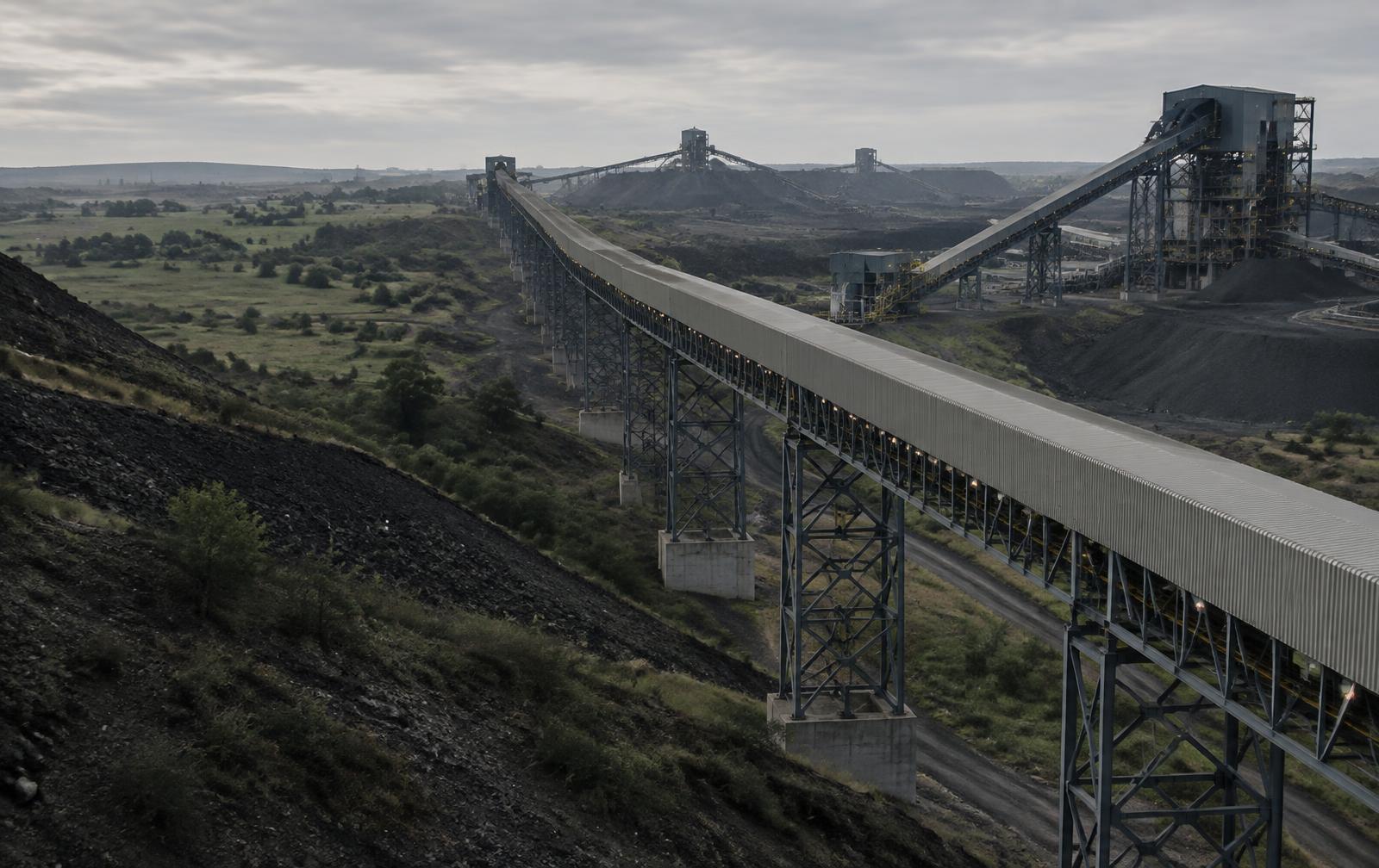 Conceptual editorial image of a coal conveyor crossing a mining landscape